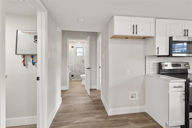 kitchen with stainless steel appliances, white cabinetry, light countertops, decorative backsplash, and light wood finished floors