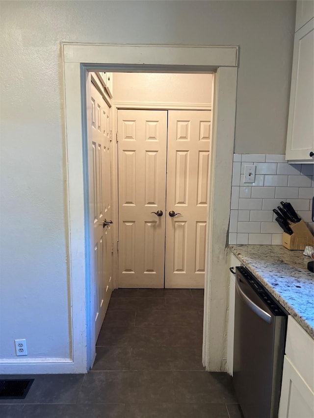 kitchen featuring visible vents, decorative backsplash, dark tile patterned floors, white cabinetry, and stainless steel dishwasher