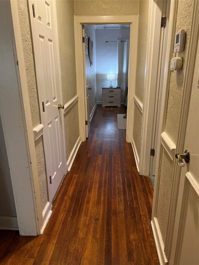 corridor featuring dark wood-type flooring and a textured wall