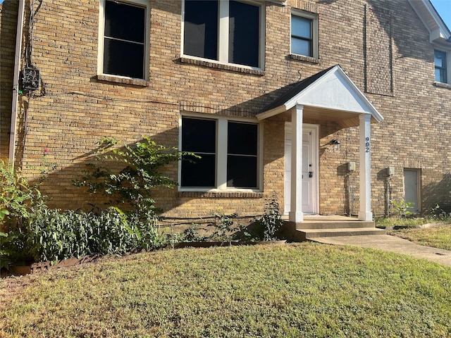 view of exterior entry featuring brick siding and a yard