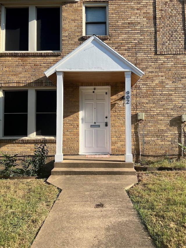 entrance to property featuring a porch and brick siding