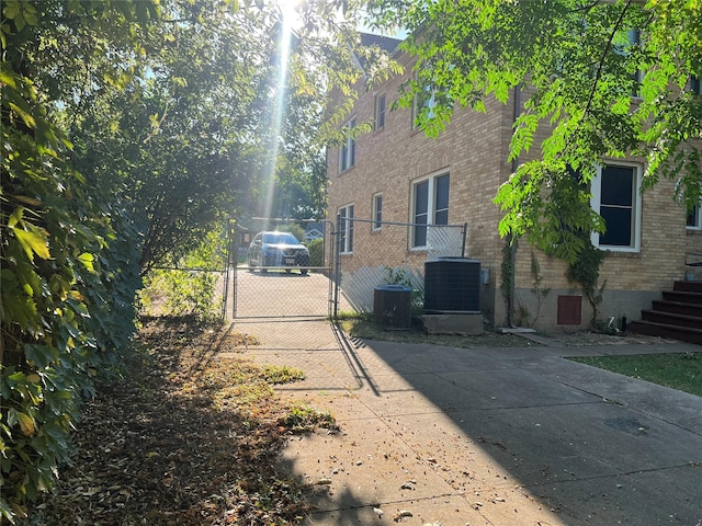 view of property exterior with brick siding, central AC unit, fence, and a gate