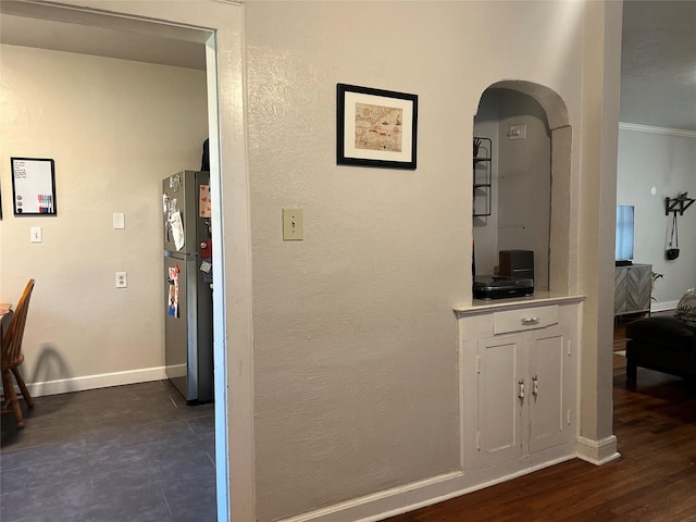 corridor featuring arched walkways, dark wood finished floors, a textured wall, ornamental molding, and baseboards