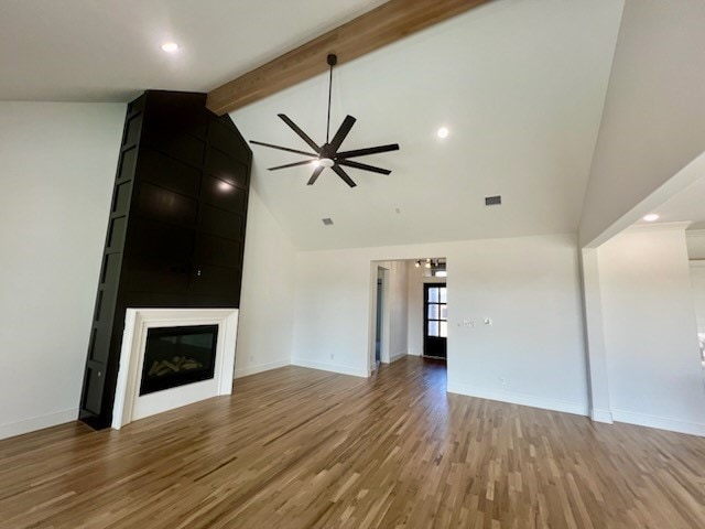 unfurnished living room with a glass covered fireplace, beam ceiling, visible vents, and light wood finished floors