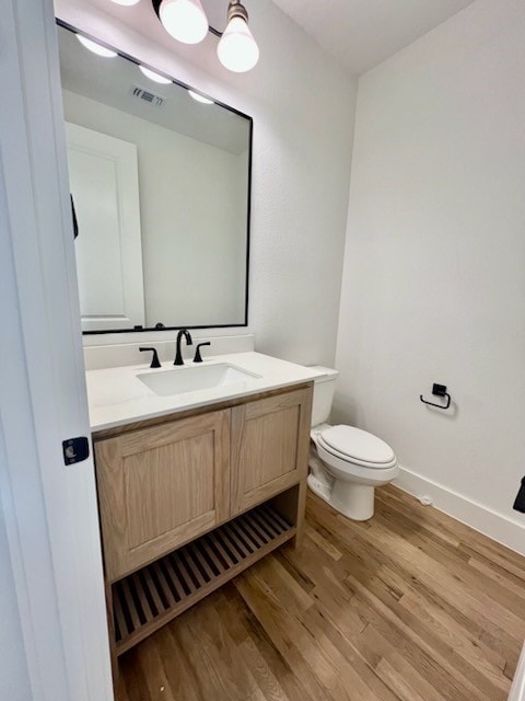 bathroom featuring baseboards, visible vents, toilet, wood finished floors, and vanity