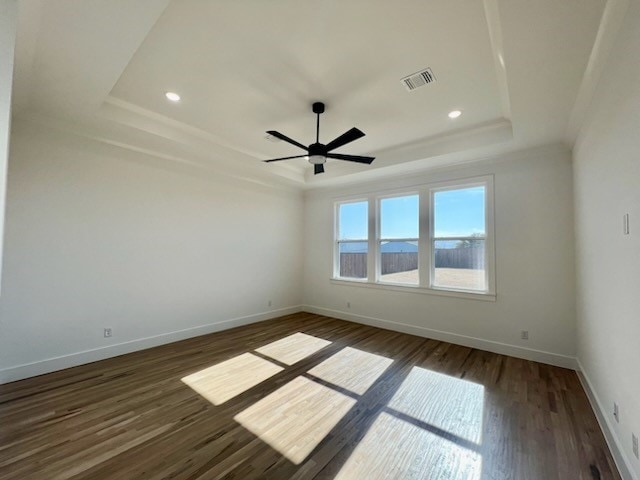 spare room featuring a tray ceiling, dark wood-style flooring, visible vents, and baseboards