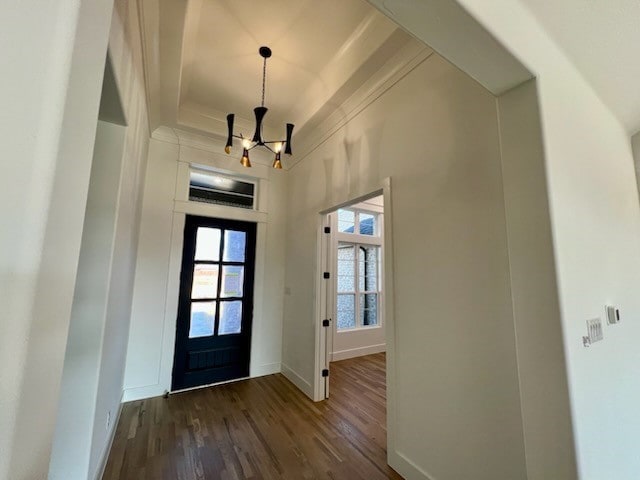 entryway with a tray ceiling, a notable chandelier, baseboards, and dark wood-style flooring