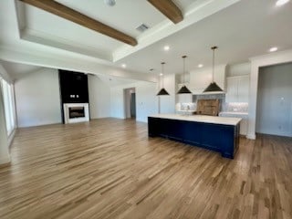 kitchen with wood finished floors, a center island, decorative light fixtures, a fireplace, and beam ceiling