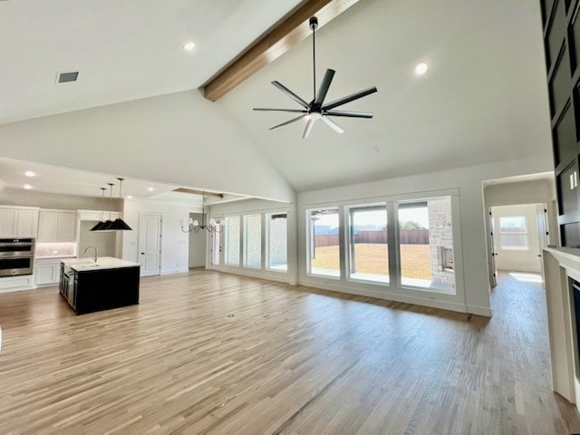 unfurnished living room featuring light wood-type flooring, a fireplace, a sink, and beamed ceiling