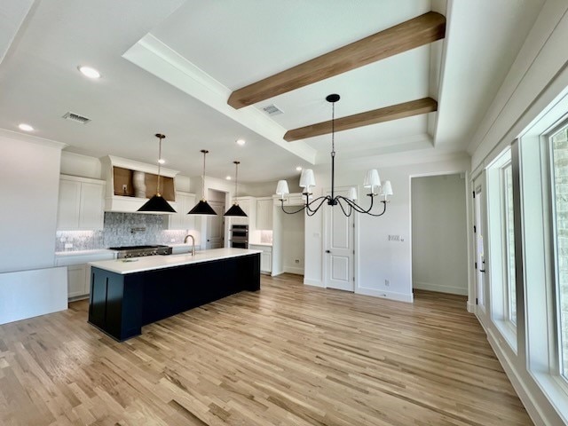 kitchen with visible vents, light wood-style flooring, a notable chandelier, light countertops, and beam ceiling