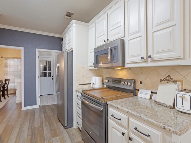 kitchen with light wood finished floors, visible vents, decorative backsplash, ornamental molding, and stainless steel appliances