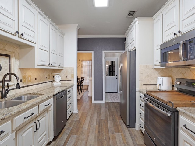 kitchen featuring visible vents, wood finished floors, stainless steel appliances, crown molding, and a sink