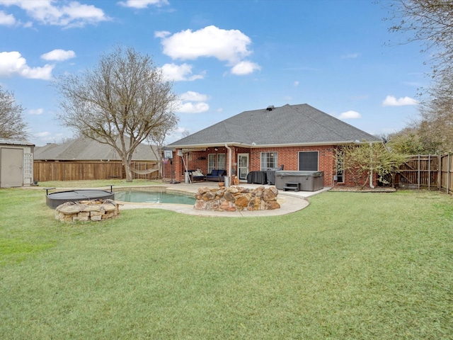 back of house with a yard, brick siding, a fenced backyard, and a hot tub