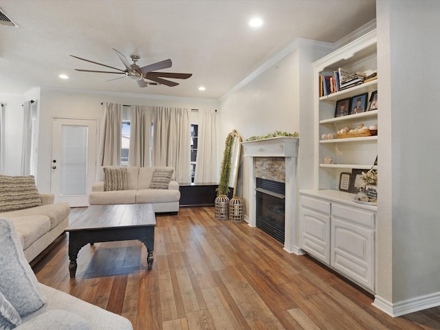 living room featuring wood-type flooring, ceiling fan, crown molding, a fireplace, and recessed lighting