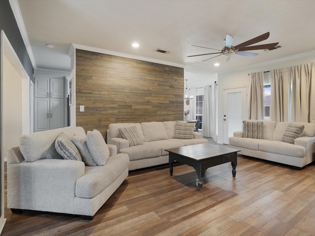 living room with an accent wall, visible vents, crown molding, and wood finished floors