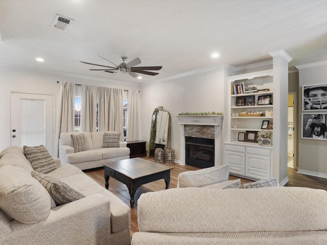 living room with a stone fireplace, wood finished floors, visible vents, and crown molding