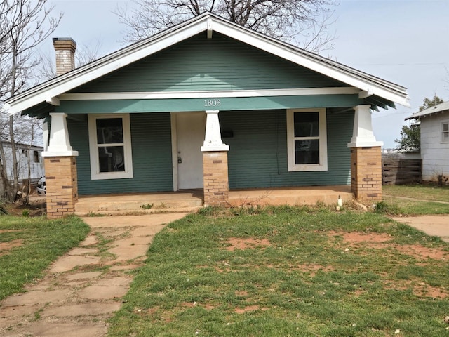 bungalow with a porch, a chimney, and a front lawn