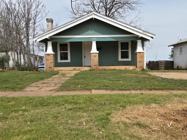 view of front facade with covered porch, a front lawn, a chimney, and brick siding