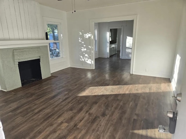 unfurnished living room with a ceiling fan, a brick fireplace, dark wood-style flooring, and baseboards