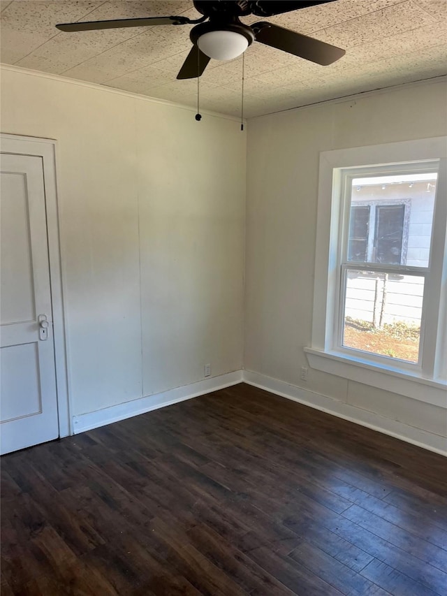 empty room with dark wood-style flooring, a ceiling fan, and baseboards