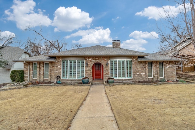 view of front of property with a shingled roof, a front yard, a chimney, and brick siding