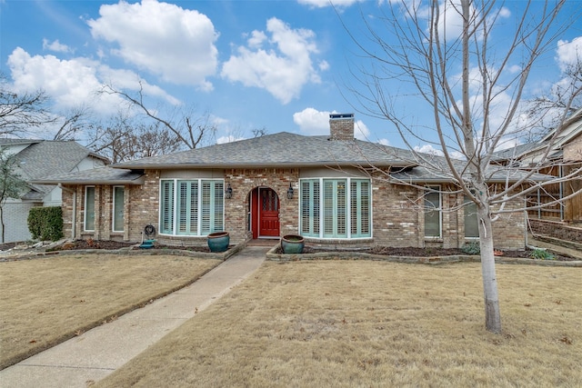 view of front of house featuring roof with shingles, a chimney, a front lawn, and brick siding