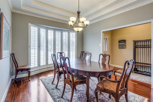 dining area with ornamental molding, a tray ceiling, dark wood-type flooring, and a notable chandelier