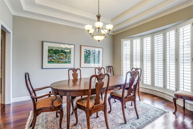 dining area with a chandelier, ornamental molding, a raised ceiling, and dark wood finished floors