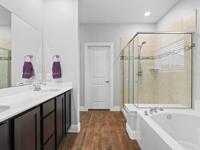 full bathroom featuring a garden tub, double vanity, wood tiled floor, a sink, and a shower stall