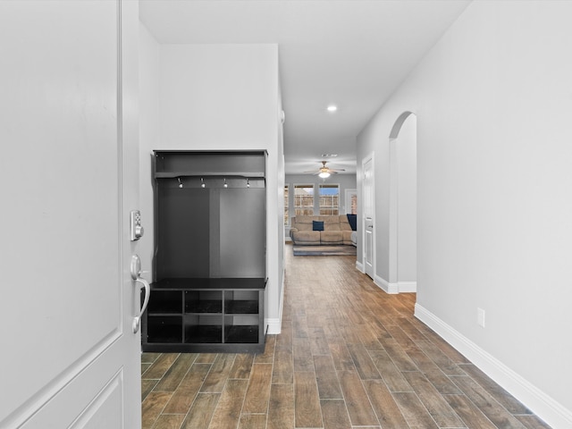 corridor with arched walkways, recessed lighting, wood finished floors, and baseboards