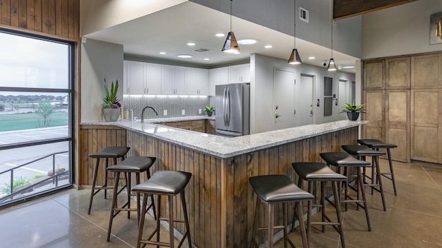 kitchen with a breakfast bar, visible vents, backsplash, freestanding refrigerator, and white cabinetry