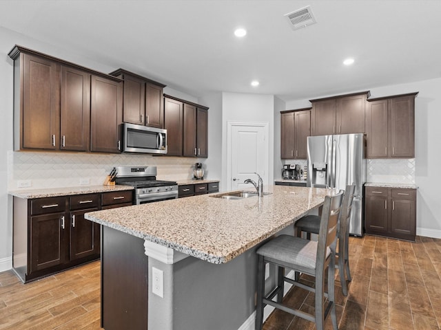 kitchen featuring dark brown cabinetry, light wood finished floors, appliances with stainless steel finishes, a kitchen bar, and a sink