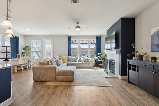 living room featuring a tiled fireplace, ceiling fan, light wood-type flooring, and visible vents