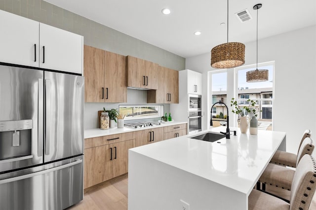 kitchen with stainless steel appliances, a sink, visible vents, light countertops, and a kitchen bar