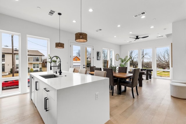 kitchen with visible vents, a sink, light wood finished floors, and a center island with sink