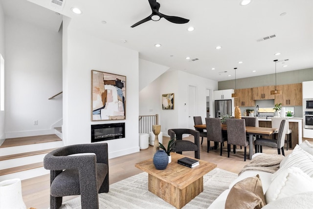 living area with visible vents, baseboards, a glass covered fireplace, light wood-style flooring, and recessed lighting