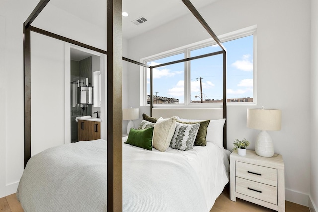 bedroom with light wood-style floors, ensuite bath, visible vents, and a sink