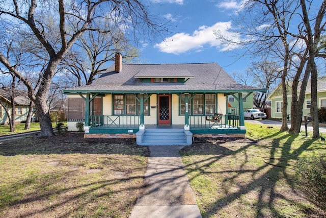 view of front of house featuring a front lawn, covered porch, roof with shingles, and a chimney