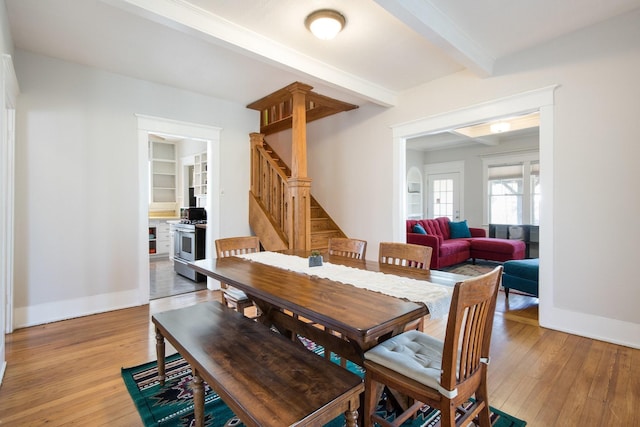 dining area featuring beamed ceiling, stairway, light wood-type flooring, and baseboards