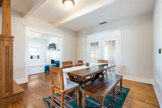 dining space featuring baseboards, beamed ceiling, a fireplace, french doors, and wood finished floors