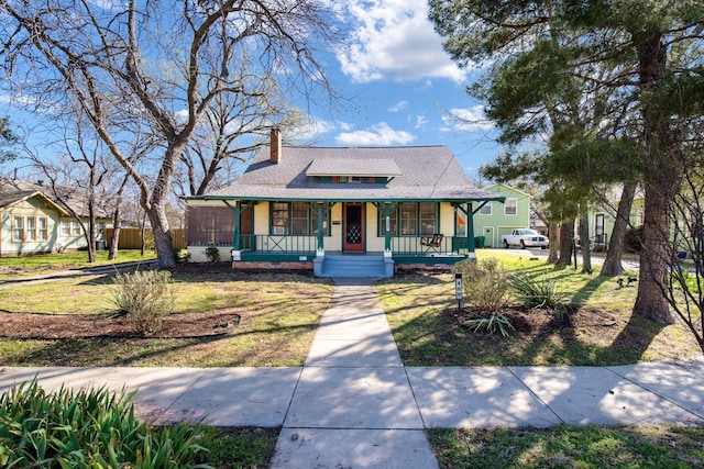 view of front of property featuring a front lawn, a porch, a chimney, and a shingled roof