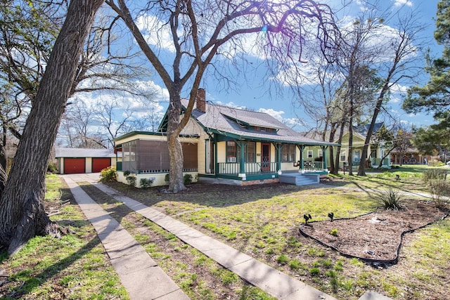 view of front of house featuring a detached garage, covered porch, an outdoor structure, a front yard, and a chimney