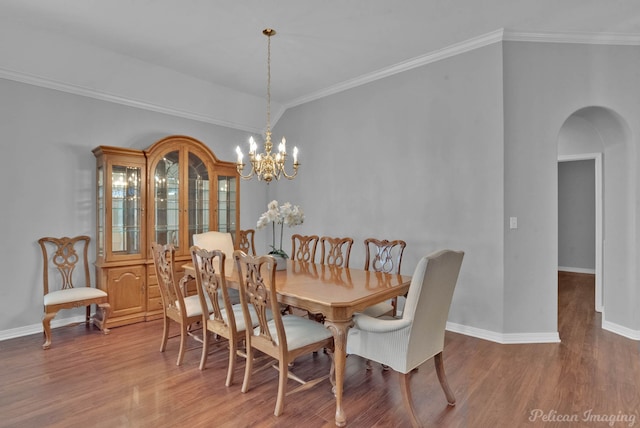 dining space featuring baseboards, ornamental molding, an inviting chandelier, wood finished floors, and arched walkways