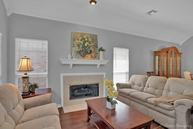 living area featuring visible vents, dark wood-type flooring, ornamental molding, lofted ceiling, and a tile fireplace