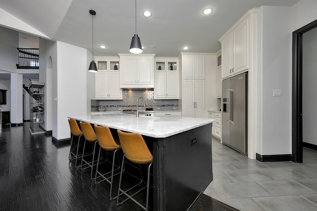 kitchen with arched walkways, light stone counters, high quality fridge, and white cabinetry