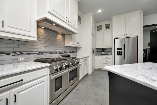 kitchen with light stone countertops, white cabinetry, washer and dryer, and premium appliances