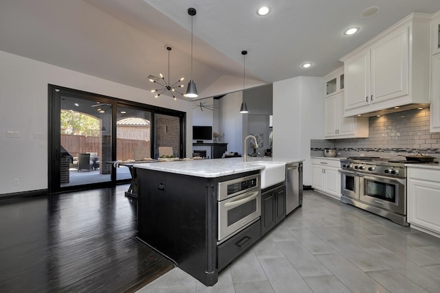 kitchen featuring lofted ceiling, a sink, white cabinetry, appliances with stainless steel finishes, and a center island with sink