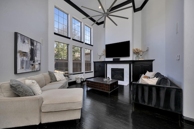 living room with ornamental molding, a glass covered fireplace, wood finished floors, and a towering ceiling