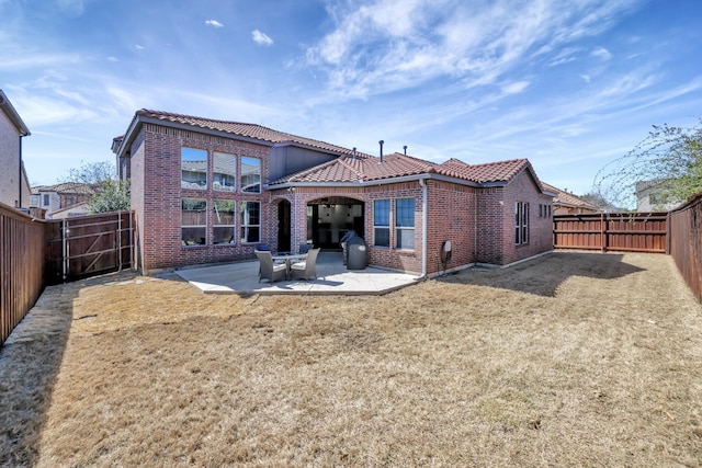 back of property featuring a patio, a fenced backyard, brick siding, a tile roof, and a yard