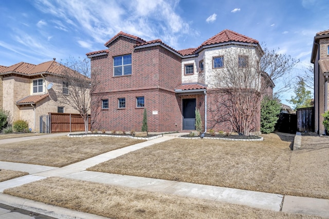 mediterranean / spanish-style house with a tile roof, fence, and brick siding